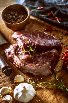 Two beef steaks on a butcher's board, surrounded by spices, herbs and garlic