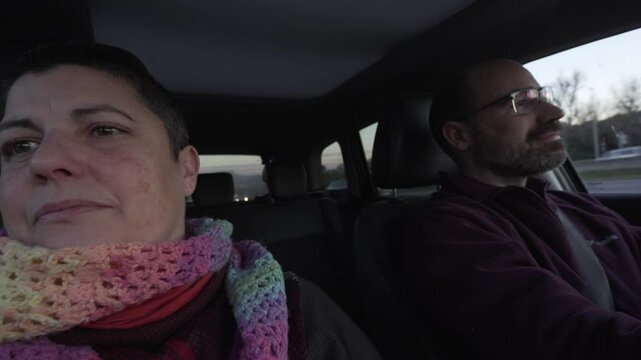 video of a couple in a car, man in his forties, bald with glasses driving, sad woman with colourful scarf and short hair