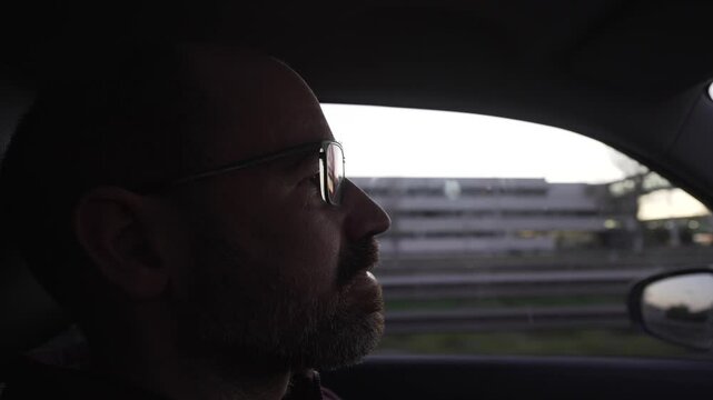 profile of a concentrated and attentive driver, a man with glasses, bald and bearded. Sunset light on his face