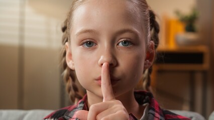 Fototapeta premium Portrait at home serious calm Caucasian little girl female daughter adopt custody child kid teenager showing hush gesture silence sign holding index finger near lips silent secret family quiet secrecy