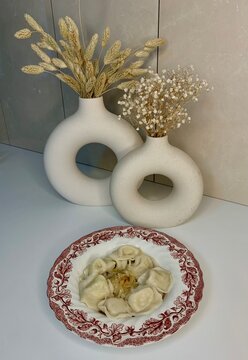 Russian pelmeni with minced meat, fried onions plus 2 vases of dried flowers. served on a plate with an uzor with oak leaves and acorns