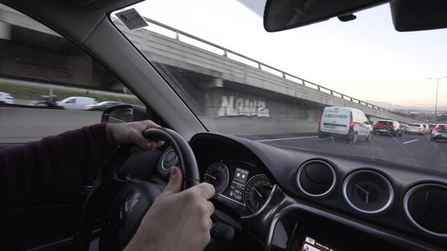 hands on a steering wheel driving in rush hour, heavy but slow-moving traffic