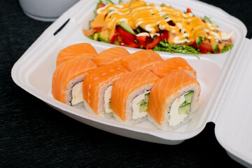 Sushi roll with salmon, cream cheese and vegetables on a white plate.