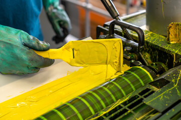 Print worker spreading yellow ink on industrial CMYK printer machine