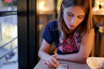 Fototapeta premium Woman Using Smartphone in a Cozy Restaurant Ambiance with Warm Lighting..