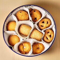 Yummy butter cookies with white paper cups in round container isolated on cream colored background from top angle view.