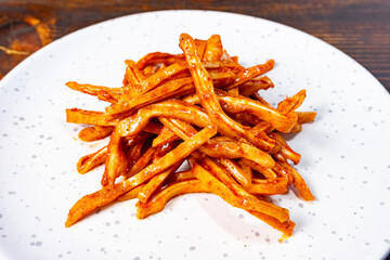 Spicy sliced pig ears on a white plate, wooden backdrop