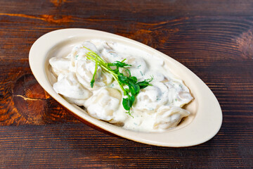 Delicious dumplings served with creamy sauce and herbs on wooden table