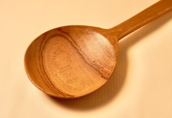 Close up brown wooden spoon kitchen utensil isolated on horizontal yellow cream colored background.