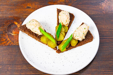 Delicious rye bread with creamy spread and pickles served on a plate