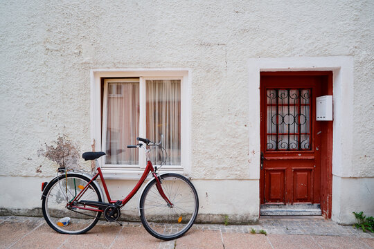 Red Bicycle Leaning Against Rustic Wall with Window and Red Door
