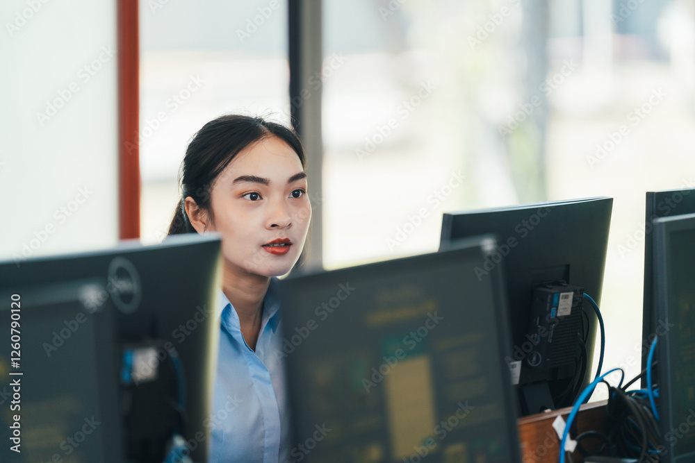 Poster professional asian woman working intently across multiple computer monitors in contemporary workspac