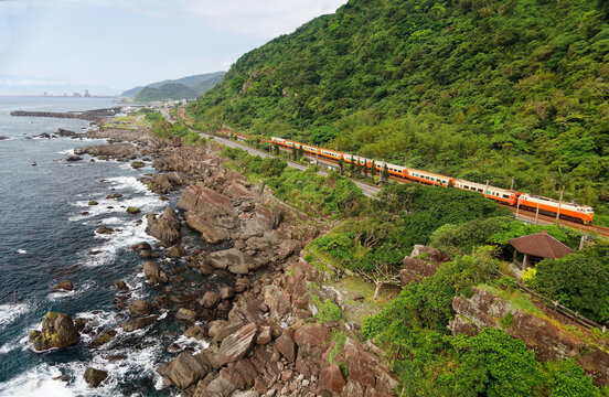 Scenery of a Chu-Kuang Express Train traveling on the railway by a coastal highway along a beautiful rocky beach under mountains of green lush forests in Beiguan Tidal Park in Toucheng, Yilan Taiwan