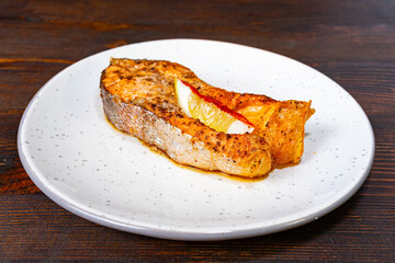 Grilled salmon steak served on a white plate with lemon slice