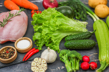 The concept of diet, detox, proper and healthy nutrition, recipes. Top view of raw turkey fillet with a sprig of rosemary lies on a black stone plank surrounded by vegetables, herbs, spices on a dark