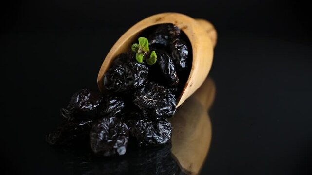 Wooden spoon with prunes and herbs on a black background.