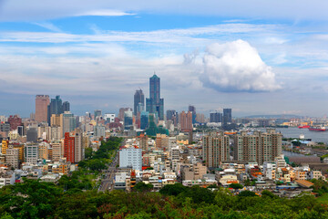 Fototapeta premium Panorama from a viewpoint overlooking vibrant Kaohsiung City in Taiwan, with ships parking in the harbor, a green avenue extending in downtown and landmark 85 Sky Tower standing under sunny cloudy sky