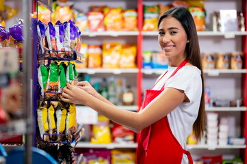 Latina woman, grocery store worker, performs different tasks inside the store. Beautiful Latina woman arranges products on the shelf for better presentation.