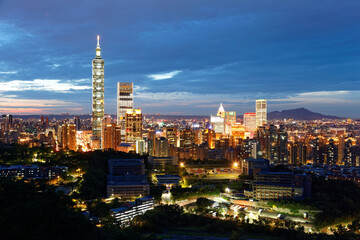 Aerial panorama of Taipei City in blue dusk, with view of Taipei 101 Tower among skyscrapers in XinYi District in downtown area and Tamsui River on distant horizon in  beautiful evening twilight