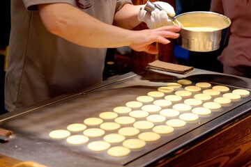 In Raohe Street Night Market, Taipei, Taiwan, a stall vendor pouring creamy batter on a hot plate to make Dorayaki, a Japanese pancake-like dessert & a street snack popular with local Taiwanese people