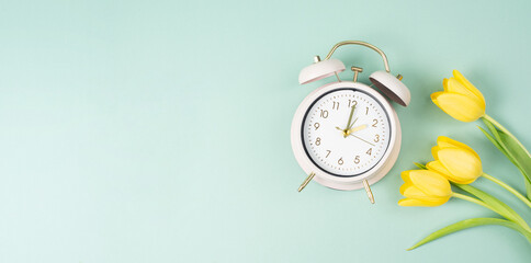 Alarm clock with yellow tulip flowers, switch to daylight saving time in spring, summer time changeover