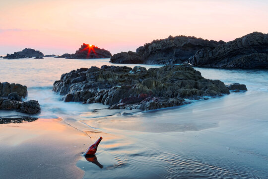 A photographer taking photos of sunrise at a rocky beach with golden sunlight reflected on the water, sea waves rushing upon the shore & Guishan Island on horizon at Wai'ao Coast, Ilan (Yilan), Taiwan - Powered by Adobe