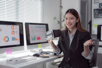 Asian businesswoman showing virtual reality headset presenting financial charts graphs and data analysis on computer screen in modern office, business and technology concept