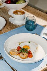 A luxurious breakfast setup on a wooden table showing fresh Mediterranean dishes creamy spreads and a hot cappuccino, bathed in natural sunlight. A perfect start to a relaxed seaside morning in Greece