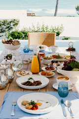 A luxurious breakfast setup on a wooden table showing fresh Mediterranean dishes creamy spreads and a hot cappuccino, bathed in natural sunlight. A perfect start to a relaxed seaside morning in Greece