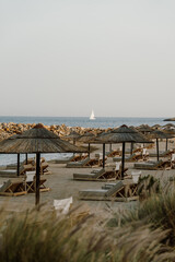 Scenic beachfront view with wooden sun loungers under straw umbrellas overlooking the calm blue ocean. Perfect for relaxation, summer vacations and tropical getaways at s luxurious resort in Greece