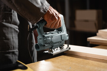 woodworking hobby. Close-up of elderly carpenter working with electric jigsaw cutting wood.