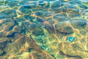 Close-up view of colorful stones beneath crystal-clear water, illuminated by sunlight at Kleopatra Beach in Alanya, Turkey. The reflection of light creates mesmerizing patterns on the submerged rocks