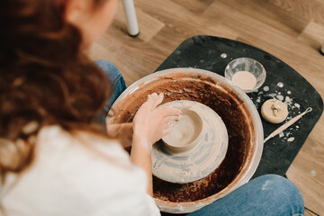 Artisan sculpts a pottery plate on the spinning wheel. Craftswoman is molding porcelain dish in the...