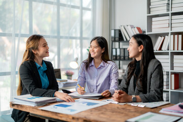 Professional Asian businesswomen analyzing financial charts, working collaboratively in sleek office environment, sharing strategic insights