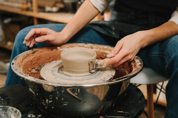 Creating ceramic earthenware on the manufacturing. Artisan forms clay pot with potters tool on the spinning wheel.
