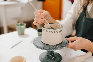 Painter is drawing and adding unique designs to the earthenware. Artist is decorating and painting handmade ceramic clay cup in the creative workshop.