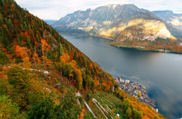 Aerial panorama from a viewpoint above Hallstatt, a peaceful lakeside village in Salzkammergut region of Austria, with colorful autumn forests on the mountains and a path winding on the mountainside