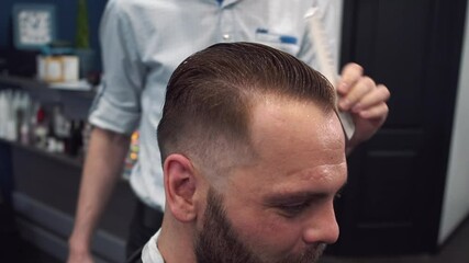 A skilled barber in a barbershop carefully combs a clients wet hair during a haircut. Precision, style, and mens grooming are showcased in every movement of the professional hairstylist. 