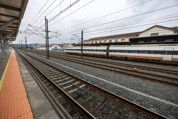 Fototapeta premium A sleek high-speed train pauses at a railway station, showcasing modern transportation against a cloudy sky and historical station architecture in the backdrop, evoking travel.