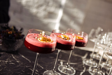 Pink sweet and sour berry cocktails with fluffy foam in elegant long-stemmed glasses. Delicious drinks are decorated with a slice of orange and flowers.