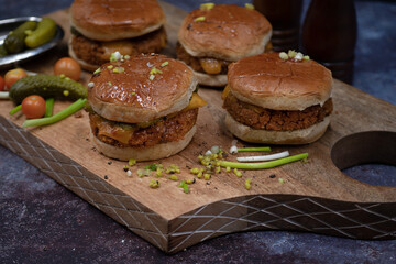 Vegan burgers made with seitan and vegan cheese, pickles on wooden cutting board
