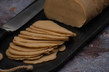 Sliced seitan lunchmeat loaf on  black slate, copy space