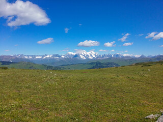 Fototapeta premium meadow against the backdrop of mountains and blue sky with clouds