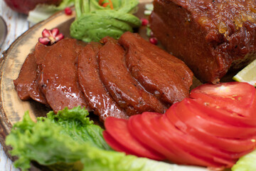 Air fried seitan ham slices, plant based meat, on wooden board along with sliced tomatoes, lettuce leaves and avocado
