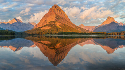Sunrise golden light panorama from the Many Glacier Hotel - reflection on Swiftcurrent Lake of...