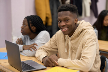 Smiling student using laptop in classroom with classmates attending lesson