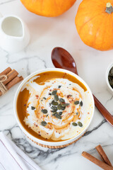 Pumpkin soup bowl with coconut milk and seeds on white marble table. Top view. Healthy homemade vegan comfort food.