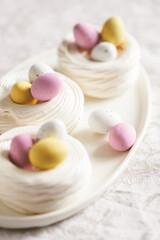 Easter meringue nests with colorful sweet eggs on plate. Easter dessert closeup.