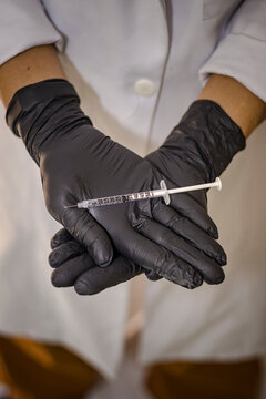 Sao Paulo, SP, Brazil - January 22 2023: Vertical photograph of a person dressed in a white coat and black gloves holding a syringe with a needle details.