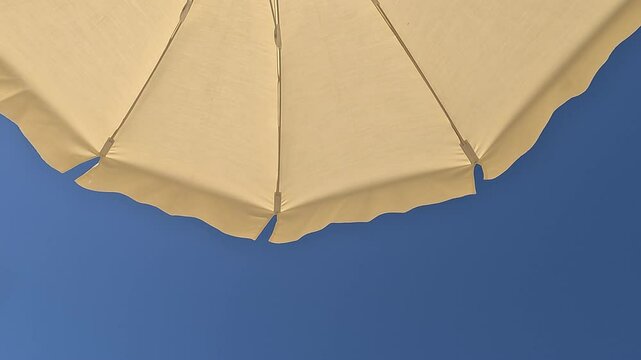 White beach umbrella. Blue sky in the background. View from below. Relaxing context. Summer holidays by the sea. General contest and location